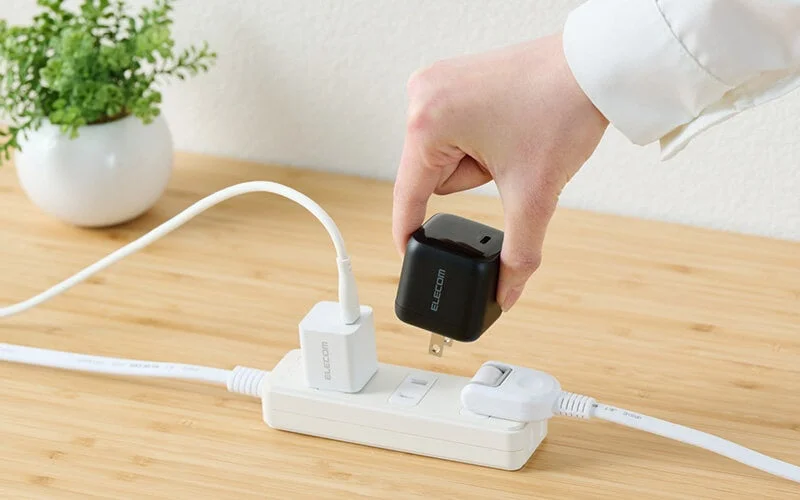 白い電源タップに黒い充電器を差し込もうとしている手の様子