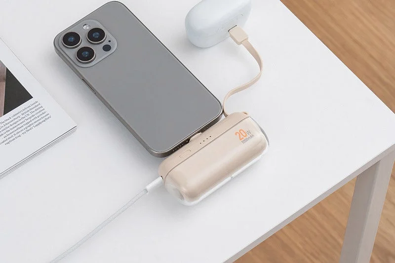 白いテーブルの上で、スマートフォンとワイヤレスイヤホンケースがモバイルバッテリーに接続され、同時に充電されている様子を捉えた画像